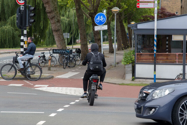 Een fatbiker rijdt hard over een druk kruispunt en laat zien dat dit gevaarlijk kan zijn voor anderen.