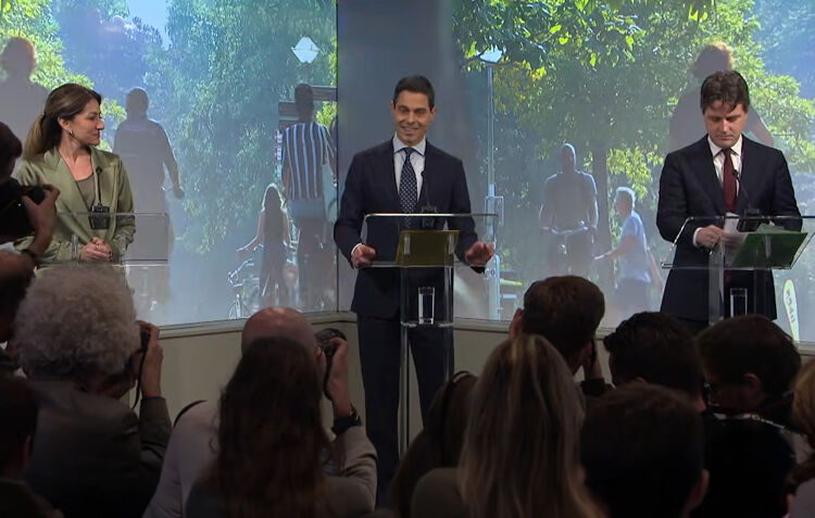 Rob Jetten presenteert het regeerakkoord aan de pers. Naast hem staan de andere leiders van de coalitie. Fotografen en journalisten luisteren aandachtig.