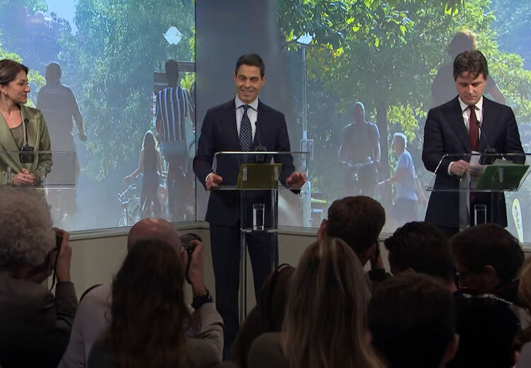 Rob Jetten presenteert het regeerakkoord aan de pers. Naast hem staan de andere leiders van de coalitie. Fotografen en journalisten luisteren aandachtig.